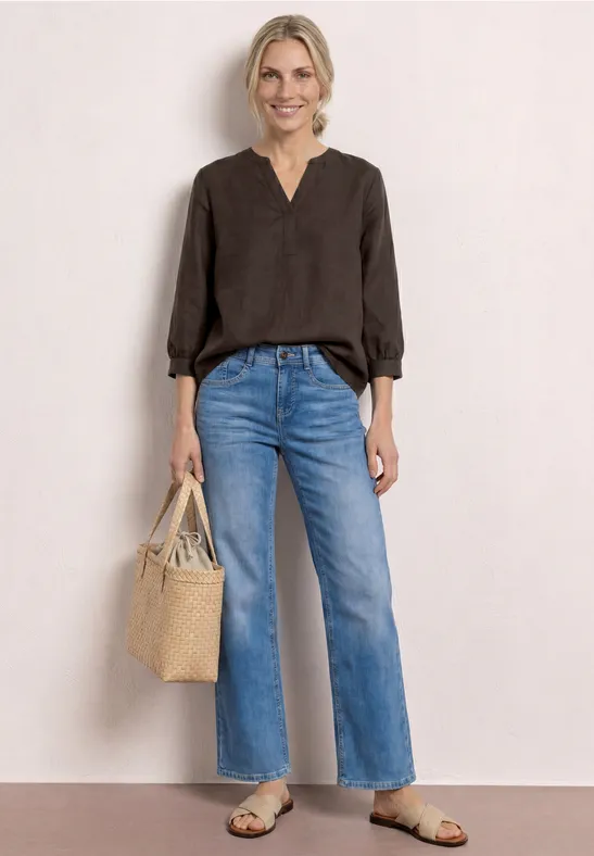 Vrouw in zwarte blouse, brede korte jeans, platte sandalen en strooien tas