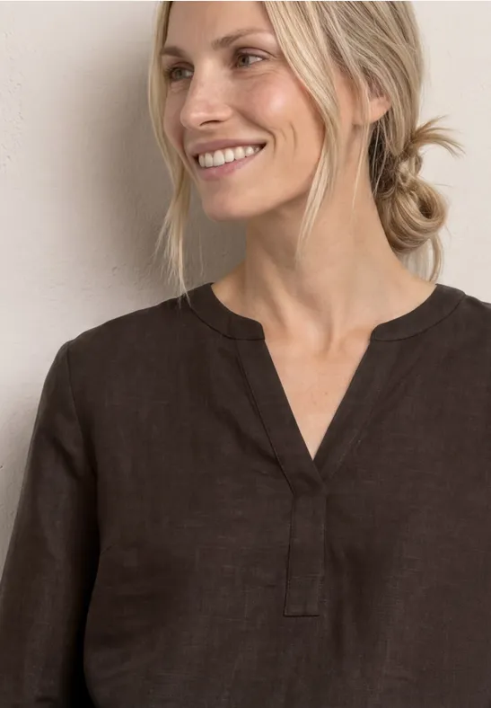 Persoon met vervaagd gezicht draagt een bruine V-hals top voor een lichte muur.