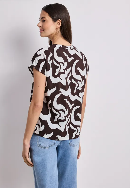 Femme de dos portant un haut à manches courtes à motif abstrait noir et blanc et un jean bleu.