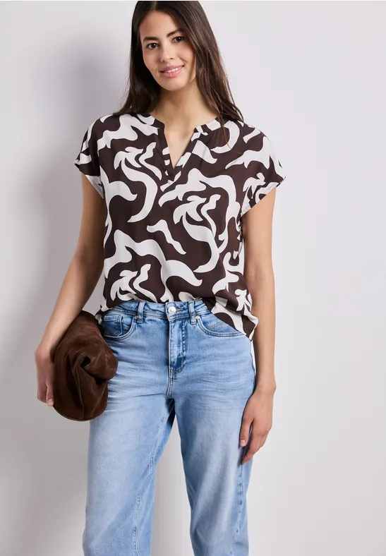 Femme en top marron à motif blanc et jean bleu, tenant une pochette marron