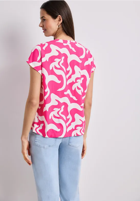 Femme de dos en haut rose et blanc à motifs et jean bleu pâle.