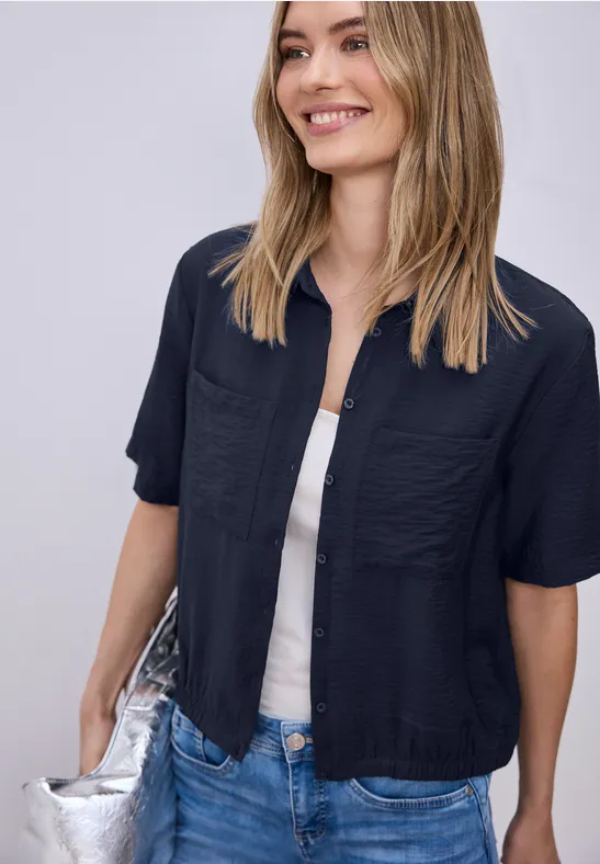 Frau trägt lässiges Outfit: schwarzes Kurzarmhemd über weißem Top, Jeans und silberne Umhängetasche.