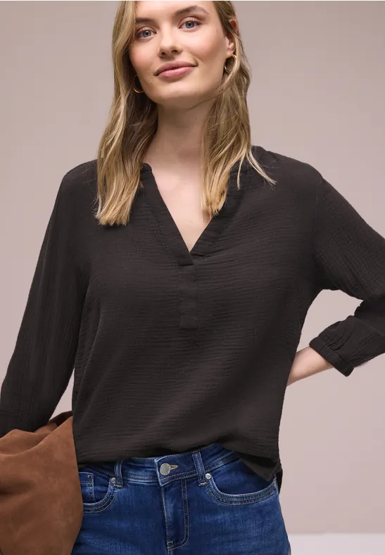 Frau in schwarzer V-Neck-Bluse und blauen Jeans, mit brauner Clutch und Hand in der Hüfte.