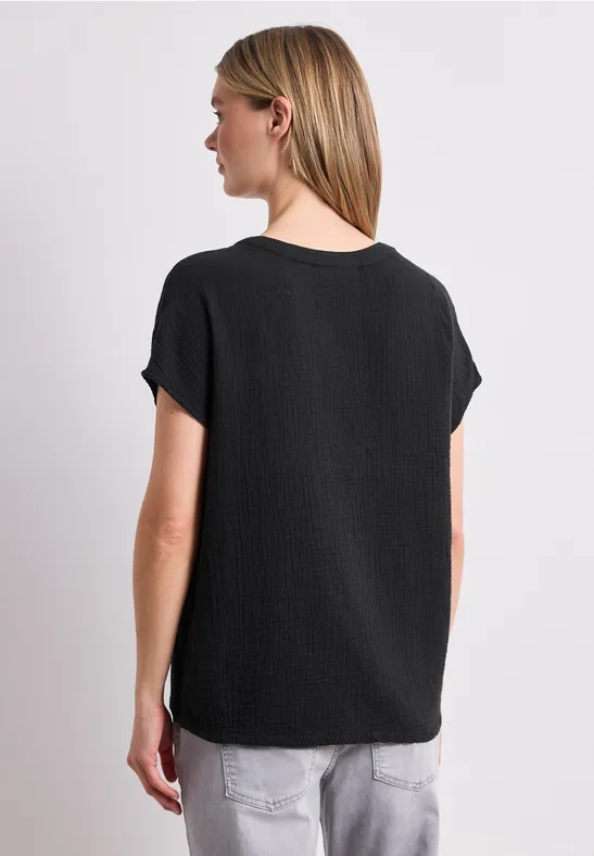 Frau von hinten in schwarzem T-Shirt und hellen Jeans vor weißem Hintergrund.