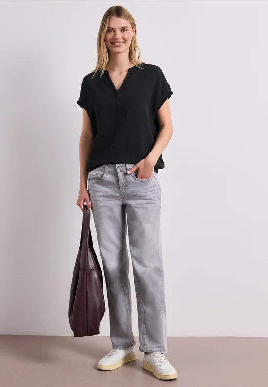 Frau trägt schwarzen V-Ausschnitt-Shirt, graue Baggy-Jeans, weiße Sneaker und hält eine große bordeauxrote Tasche.