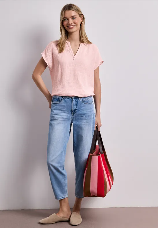 Eine Frau trägt eine rosa Bluse, blaue Jeans und hält eine rote Tasche.