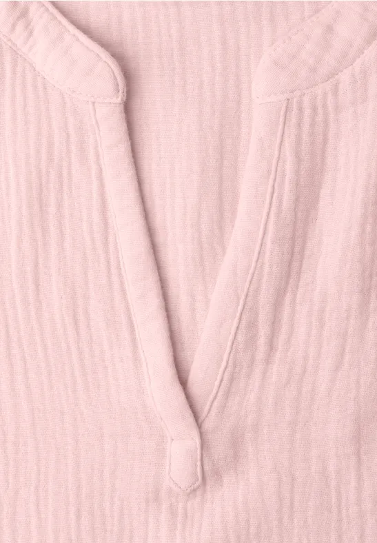Nahaufnahme eines rosa Hemdes aus leichtem Stoff mit V-Ausschnitt und dekorativem Knopfdetail.