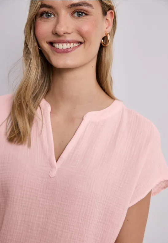 Frau in rosa kurzärmeliger Bluse mit kleinem Kragenausschnitt, blonde Haare, goldene Ohrringe