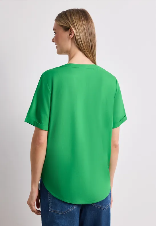 Vrouw van achteren in groen t-shirt en spijkerbroek voor een witte achtergrond.