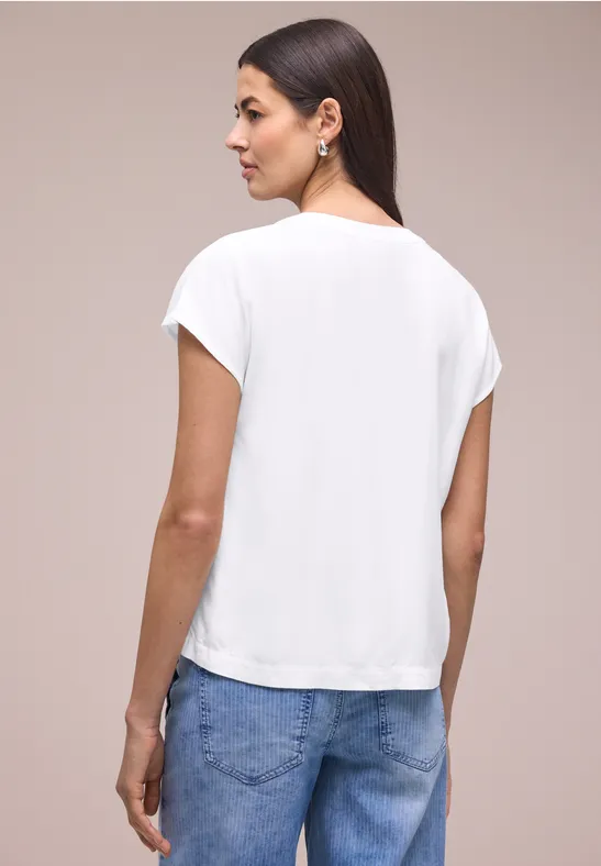 Vrouw van achteren in wit T-shirt en blauwe jeans tegen een neutrale achtergrond.