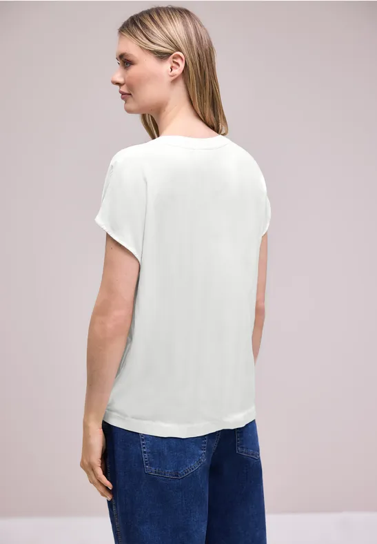 Femme vue de dos portant un t-shirt blanc et un jean bleu sur fond neutre.