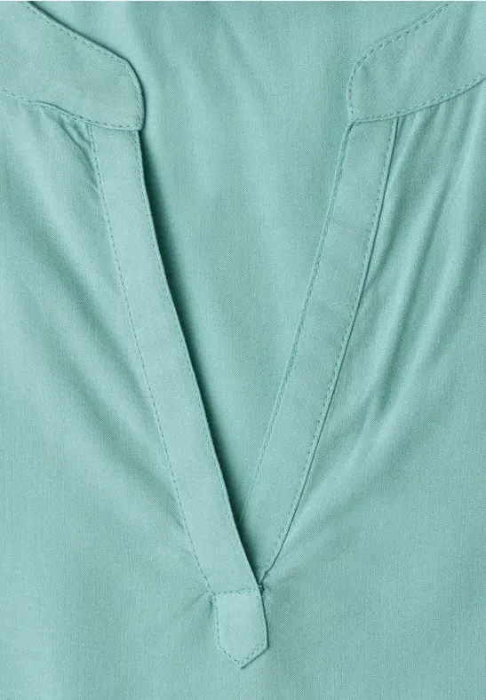 Detailaufnahme eines tealfarbenen Oberteils mit V-Ausschnitt und sichtbaren Nähten.