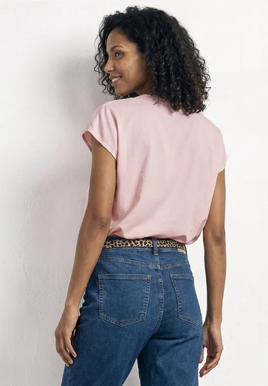 Een persoon van achteren met een roze shirt, blauwe spijkerbroek en een luipaardprintriem.