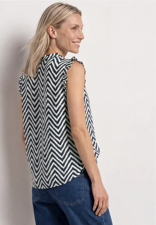 Vrouw draagt mouwloze zwart-witte chevron top, gezien van achteren, met een blauwe jeans.