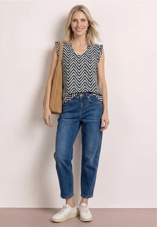 Vrouw in mouwloze zigzagtop, jeans, witte sneakers, bruine schoudertas
