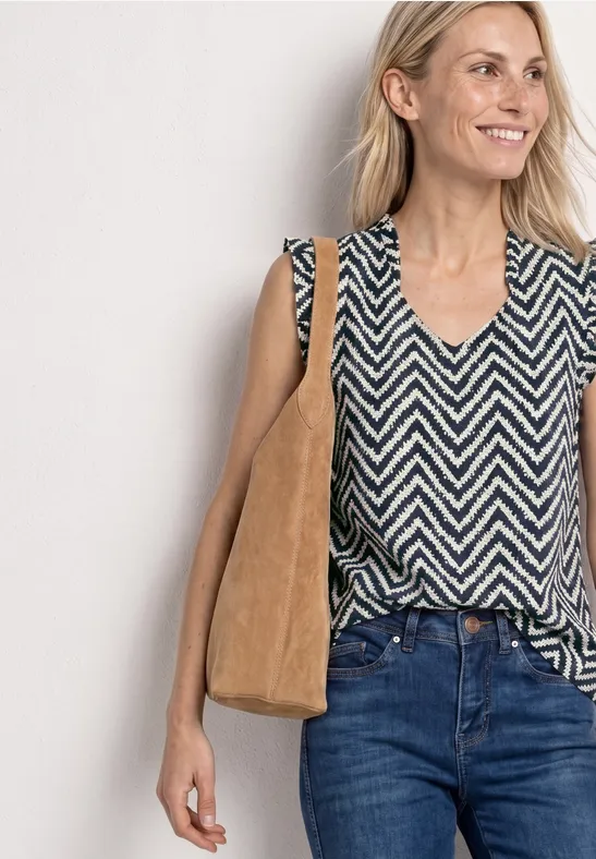 Vrouw in zwart-wit zigzagshirt, blauwe jeans en beige suède schoudertas