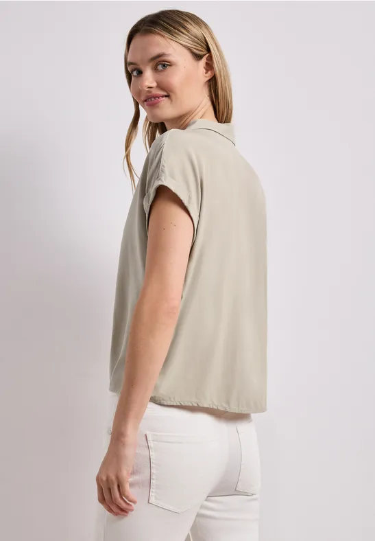 Eine Frau in beige T-Shirt und weißen Hosen, seitlich von hinten fotografiert.