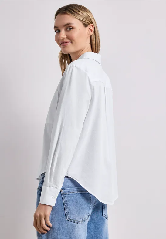 Seitliche Ansicht einer Person in weißem Hemd und Jeans vor hellem Hintergrund.