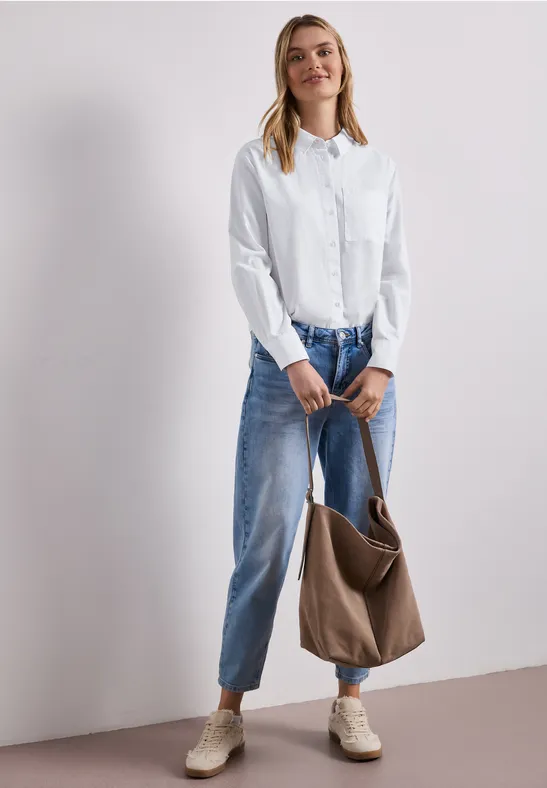 Frau trägt weiße Bluse, weite blaue Jeans, beige Schuhe und hält eine braune Tasche.