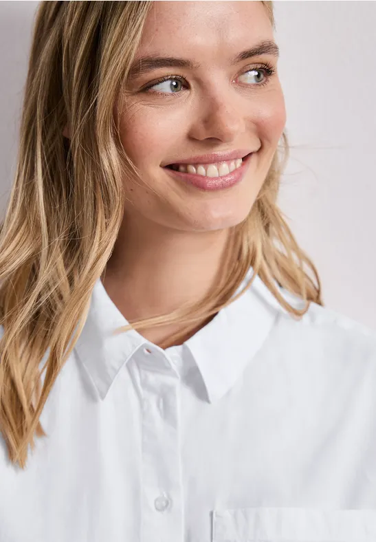 Frau mit weißer Hemdbluse, Halskette und verwischtem Gesicht vor heller Wand