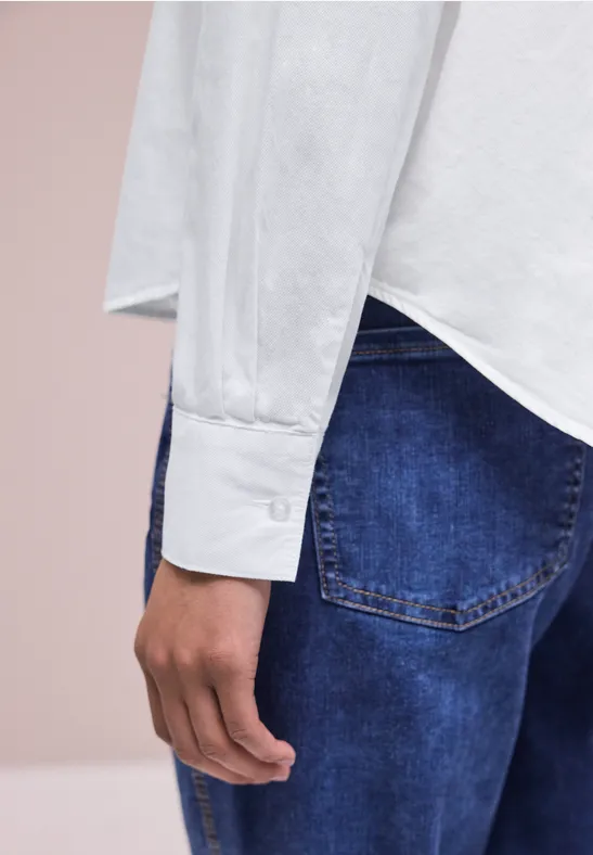 Seitliche Ansicht einer Person in weißem Hemd mit Manschette und blauen Jeans.