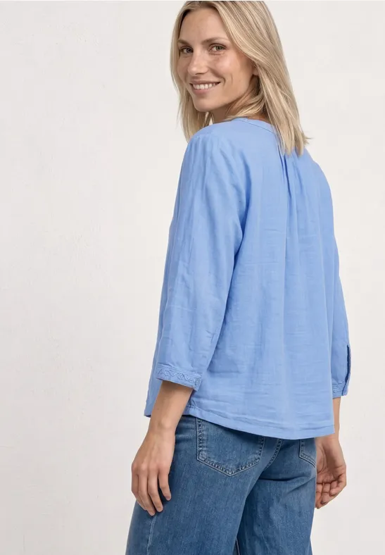 Frau von hinten in hellblauer, lockerer Bluse mit Dreiviertelärmeln und Jeans.