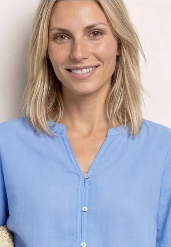 Frau mit schulterlangem blondem Haar in hellblauem Hemd vor hellem Hintergrund