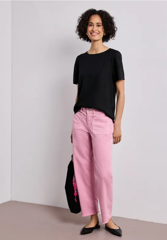 Person trägt schwarzes T-Shirt, pinke Hose, schwarze Ballerinas und schwarze Tasche.