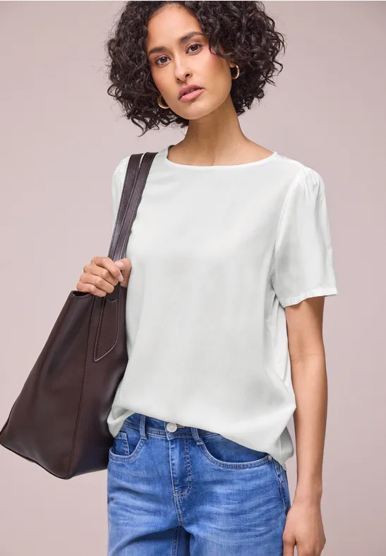 Vrouw met witte blouse, blauwe jeans en grote bruine schoudertas voor neutrale achtergrond.