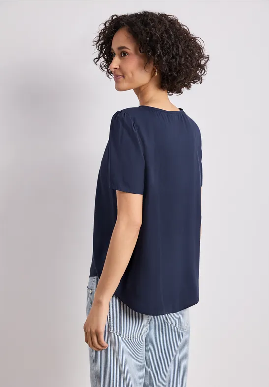 Frau von hinten in dunkelblauer, kurzärmeliger Bluse und hellen Jeans