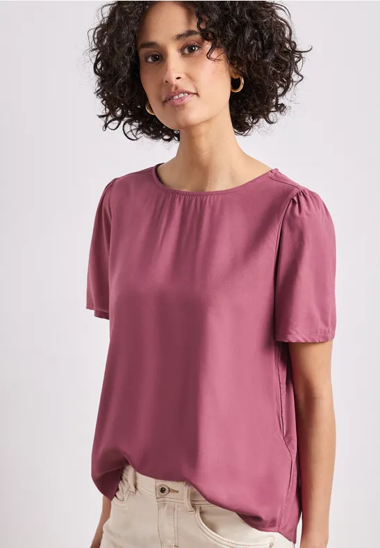Model draagt een roze korte mouwen blouse met ronde hals en vloeiende stof.