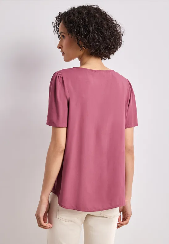 Vrouw van achteren in een roze shirt met korte mouwen en een beige broek.