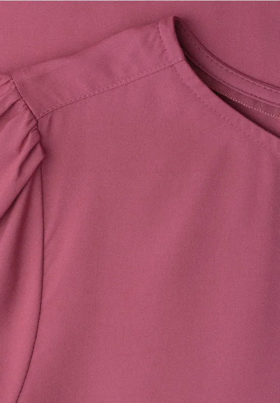 Close-up van een roze shirt met subtiele geplooide mouwen.