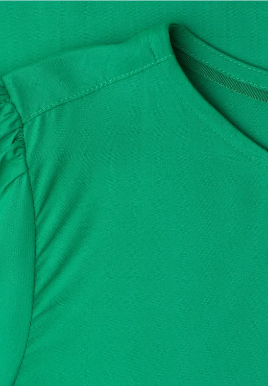 Gros plan d'un T-shirt vert à col rond avec manches légèrement froncées.