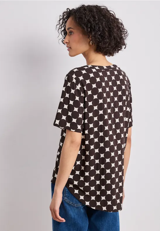 Femme aux cheveux bouclés portant un T-shirt noir à étoiles blanches et un jean, vue de dos.