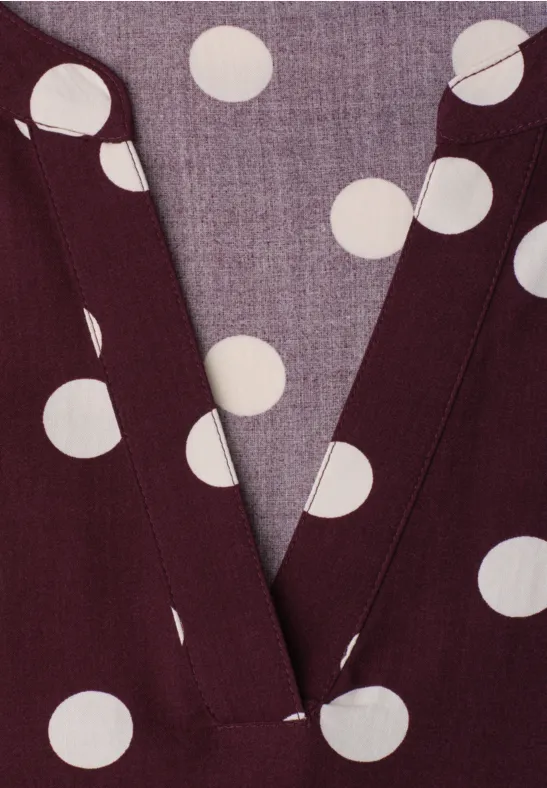 Nahaufnahme eines weinroten V-Ausschnitt-Oberteils mit weißen Polka-Dots.