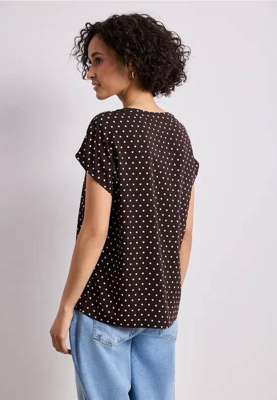 Rückansicht einer Person in schwarzem, weiß gepunktetem T-Shirt und blauen Jeans