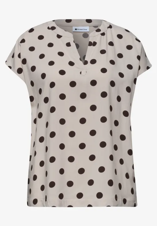 Beige blouse met zwarte polkadots en korte mouwen.