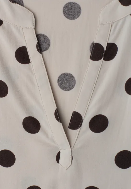 Close-up van een lichtbeige top met zwarte polka dots en V-hals.