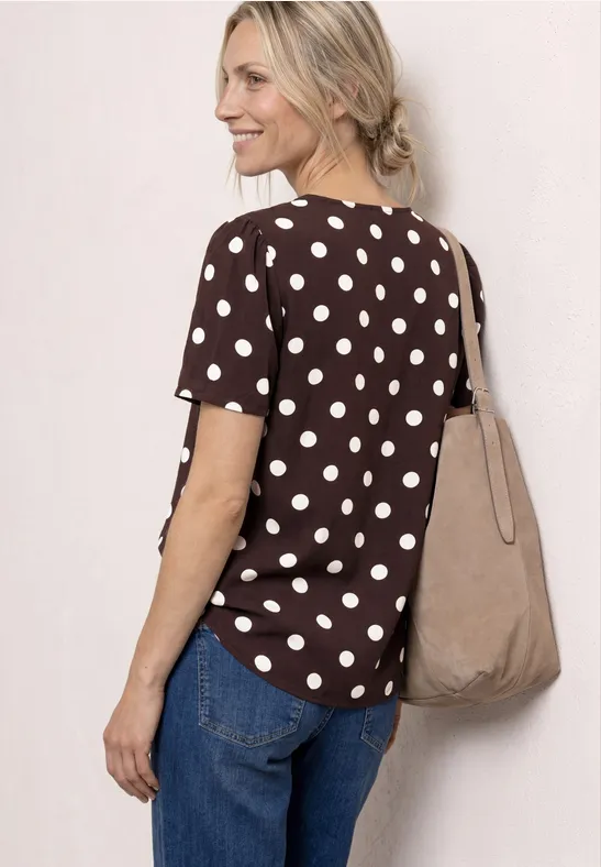 Frau von hinten in braunem Tupfen-Shirt, blauen Jeans und beiger Stofftasche.