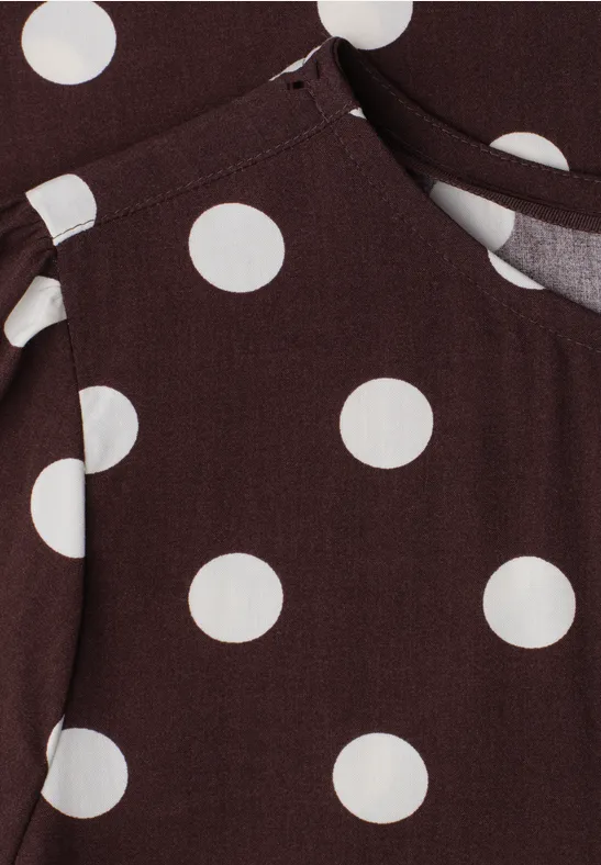 Brauner Stoff mit großen weißen Punkten und einer Naht, vermutlich Teil eines Kleidungsstücks mit Tasche.