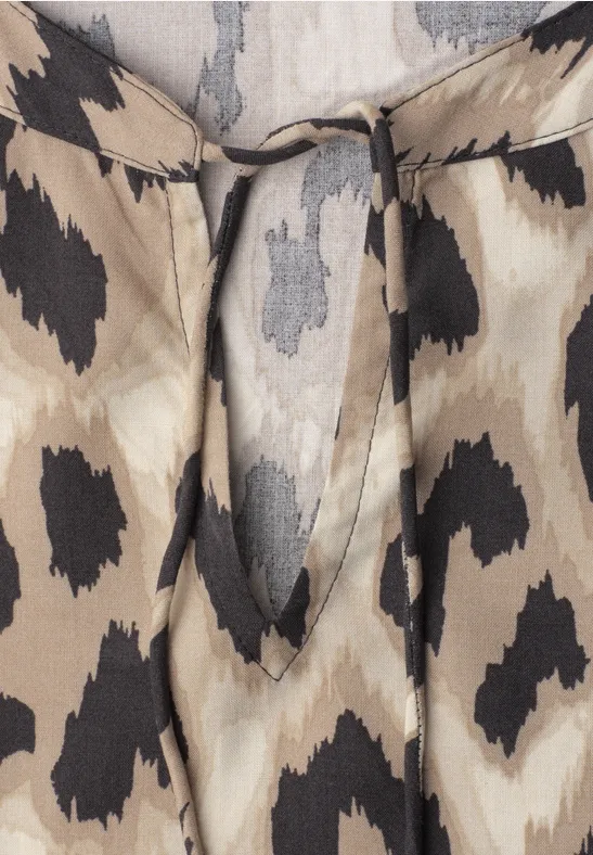 Close-up van een beige licht stoffen top met zwart gespikkeld patroon en een fijn bindbandje bij de hals.