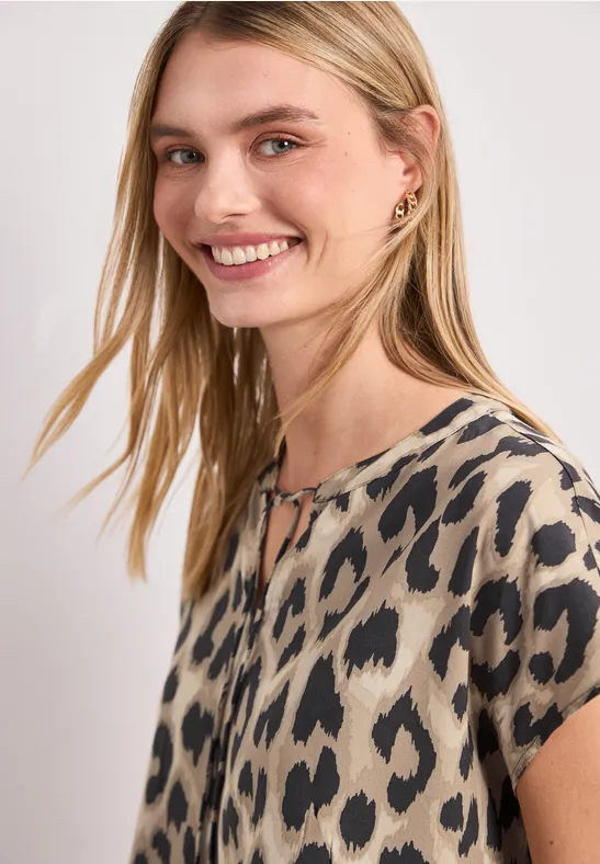 Beige blouse met korte mouwen en onregelmatig zwart vlekkenpatroon.