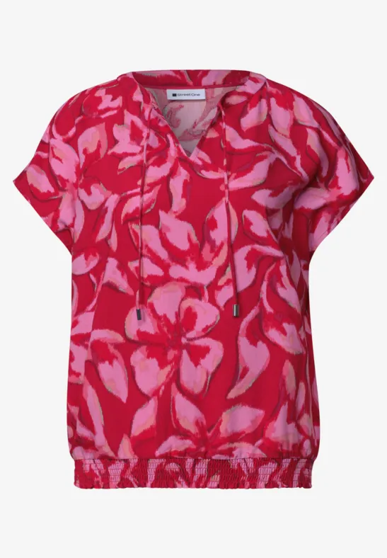 Roze blouse met rode, abstracte bloemenprint, V-hals en tunnelkoord aan de taille.