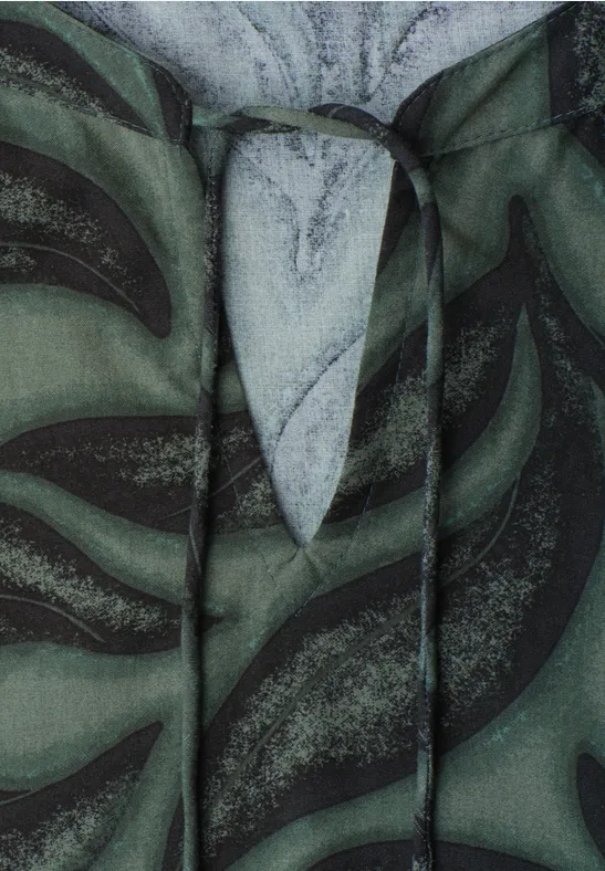 Close-up van een groene capuchontrui met zwart bladpatroon en witte accenten.
