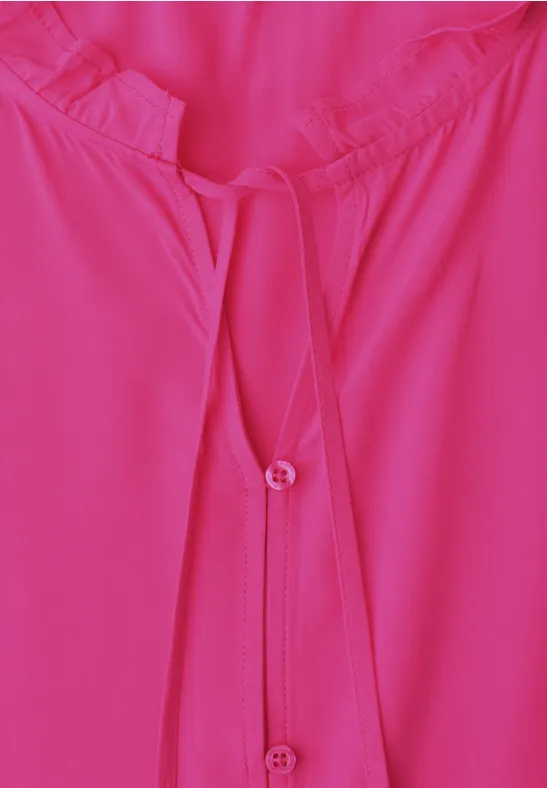 Close-up van een fuchsia roze blouse met ronde hals en knoopsluiting.