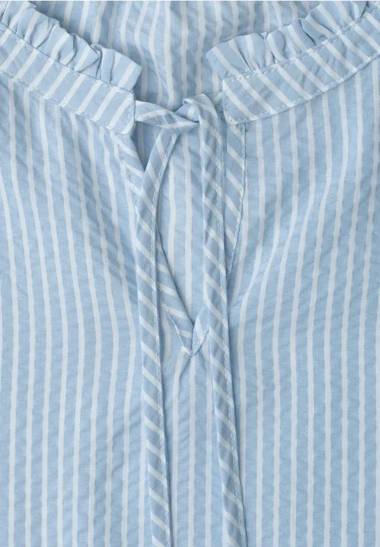 Hellblaue Bluse mit weißen Streifen und Bindeband am gerüschten Ausschnitt.