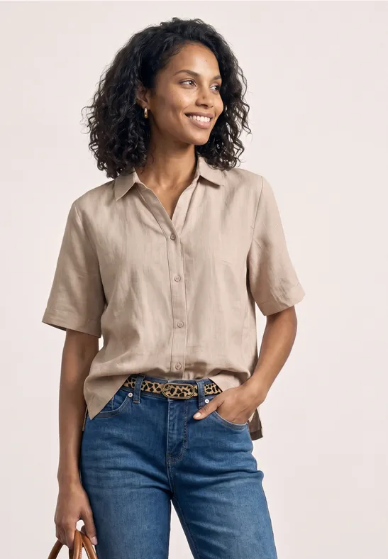 Vrouw in een beige korte mouwen blouse en blauwe jeans met luipaardenriem.