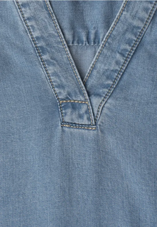 Close-up van een lichtblauw denim top met een opvallende V-neknaad.