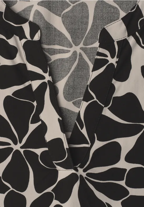 Close-up van een top met V-hals en groot zwart bloemdessin op witte stof.